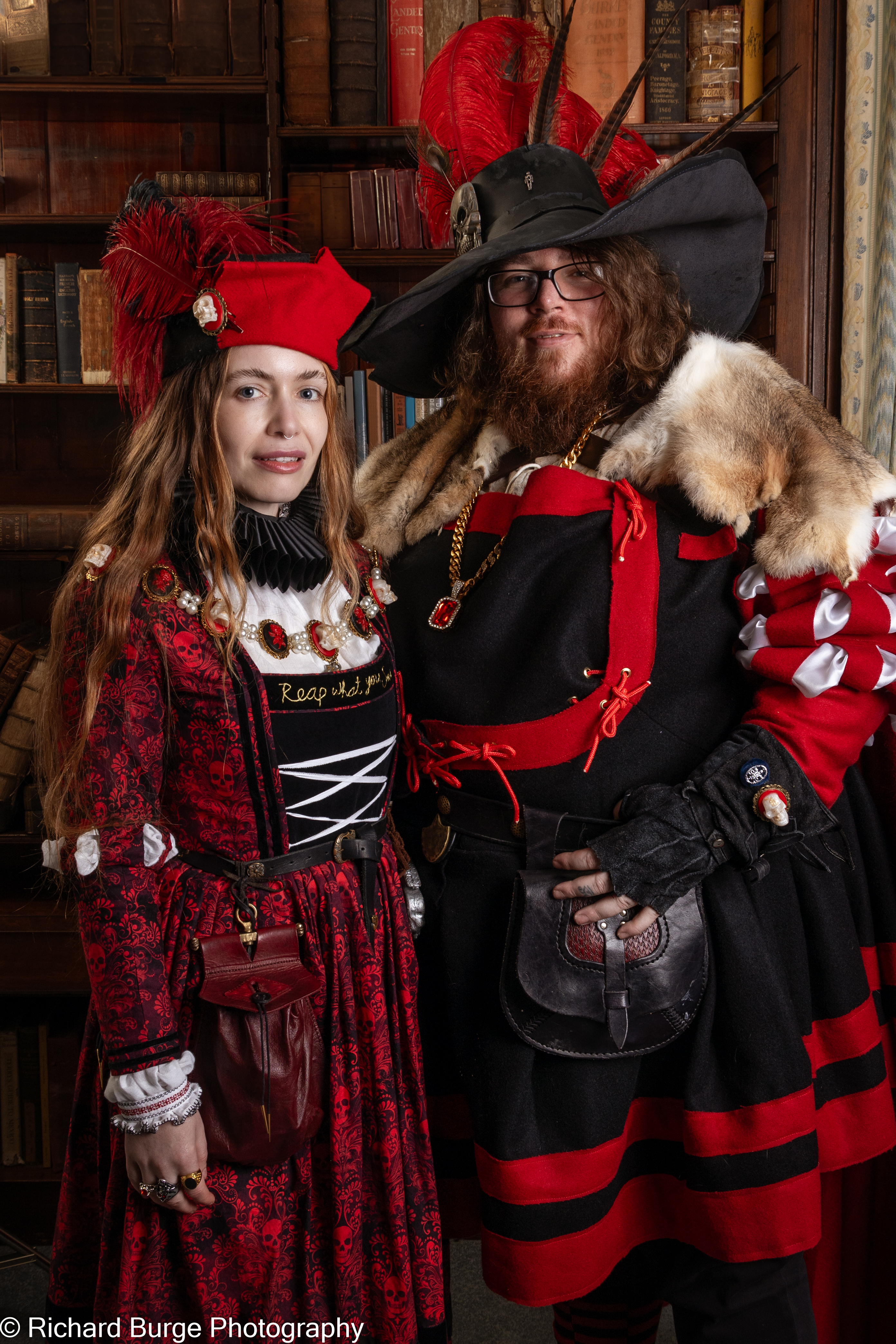 two characters from the League in Empire dresssed in red and black costume posing in front of a bookshelf with small smiles